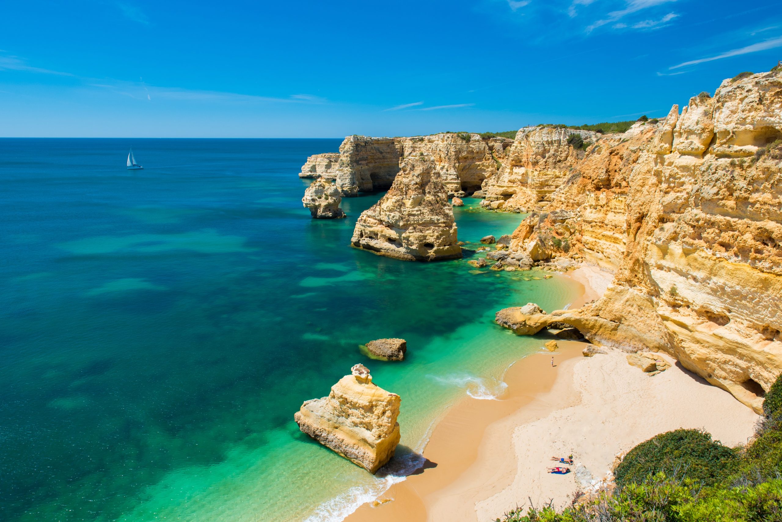 Algarve beach with golden cliffs, turquoise sea and a sailing boat offshore
